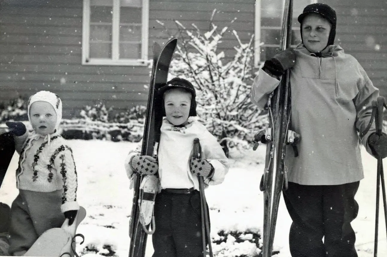 Three people with skis in snowy yard.