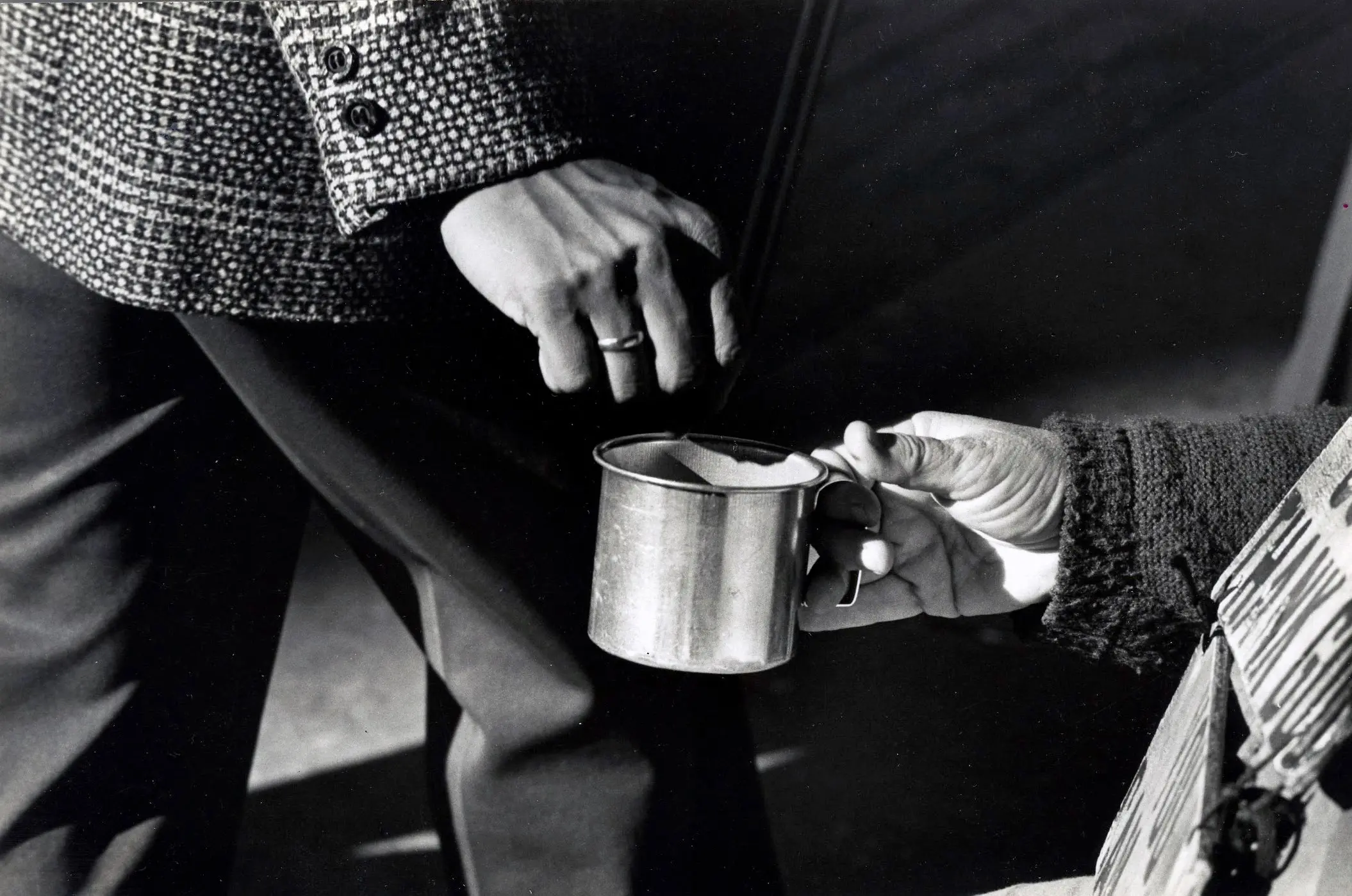 Person holding cup towards passerby in street.