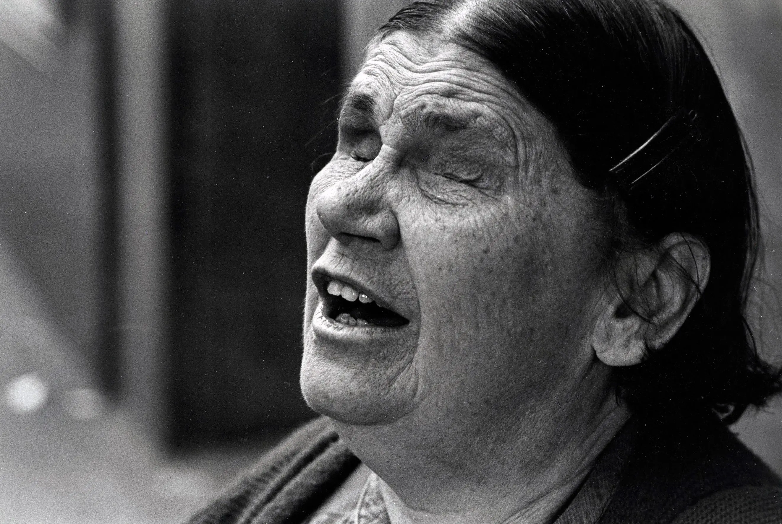 Elderly woman with eyes closed, singing passionately.