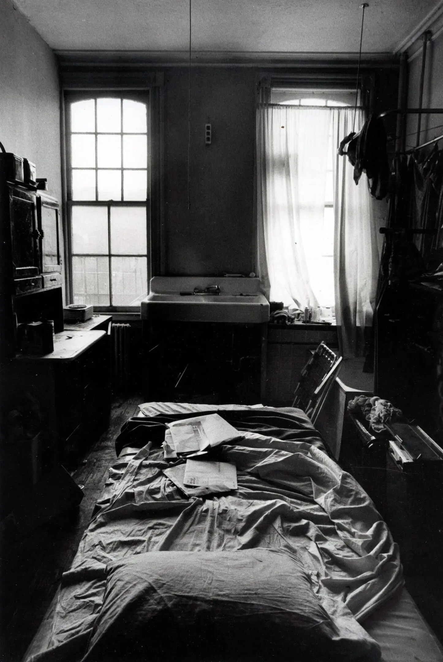 Dimly lit, cluttered room with unmade bed.