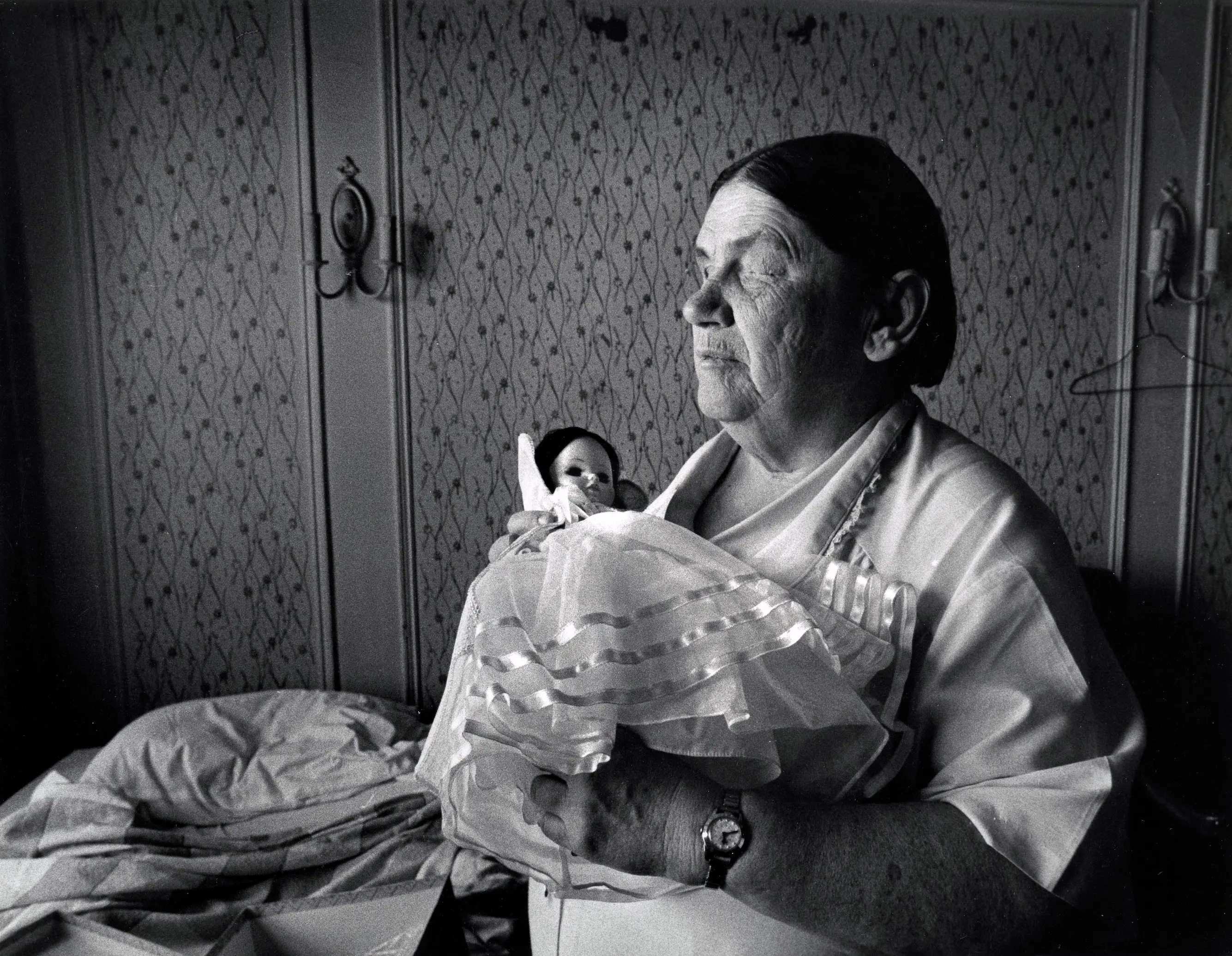 Elderly woman holding a doll, looking contemplative.