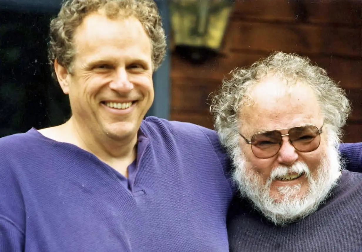 Two smiling men in purple shirts outdoors.