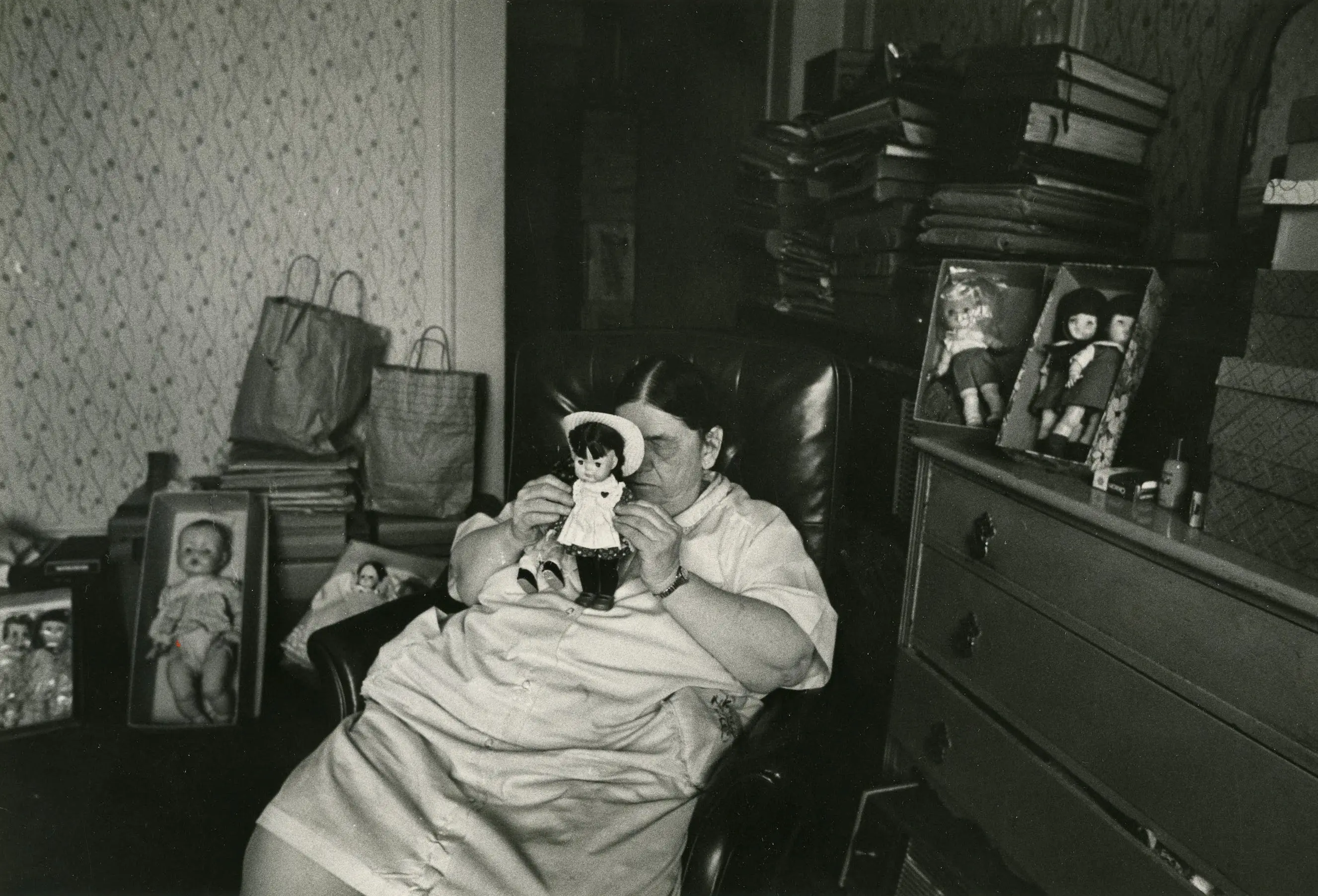 Woman holding doll in cluttered room.