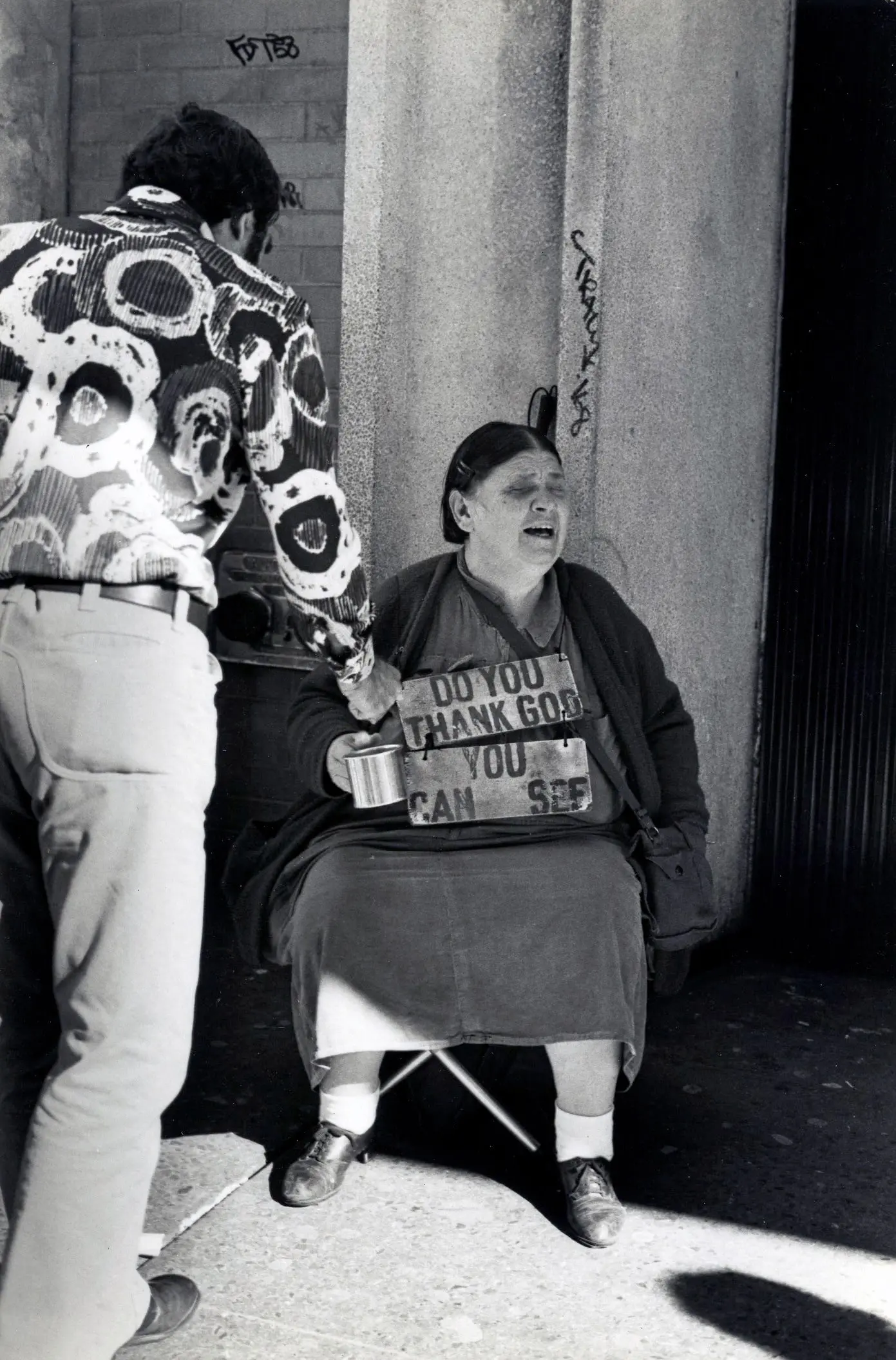 Man giving donation to seated woman outside.