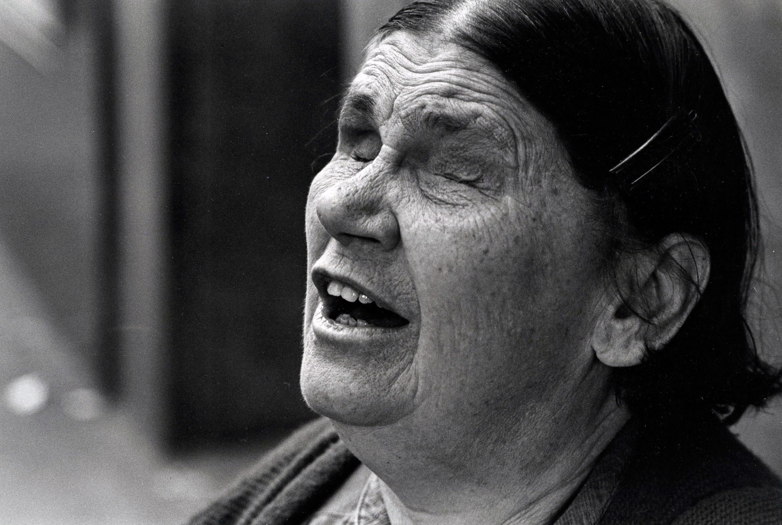 Elderly woman with eyes closed, singing passionately.