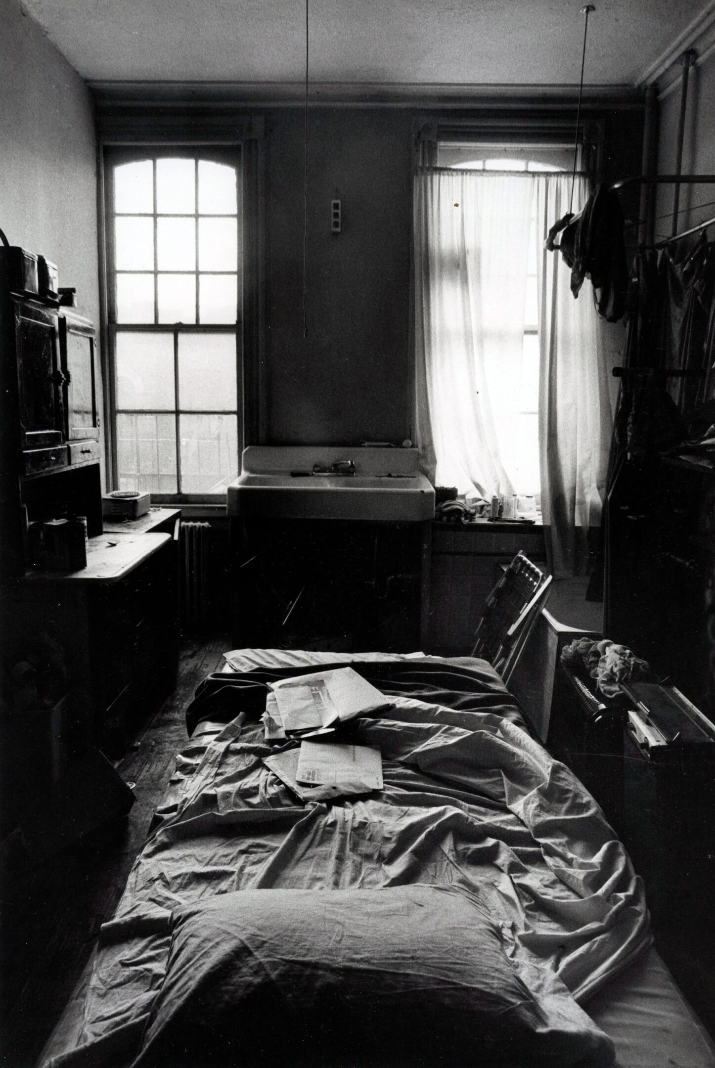 Dimly lit, cluttered room with unmade bed.