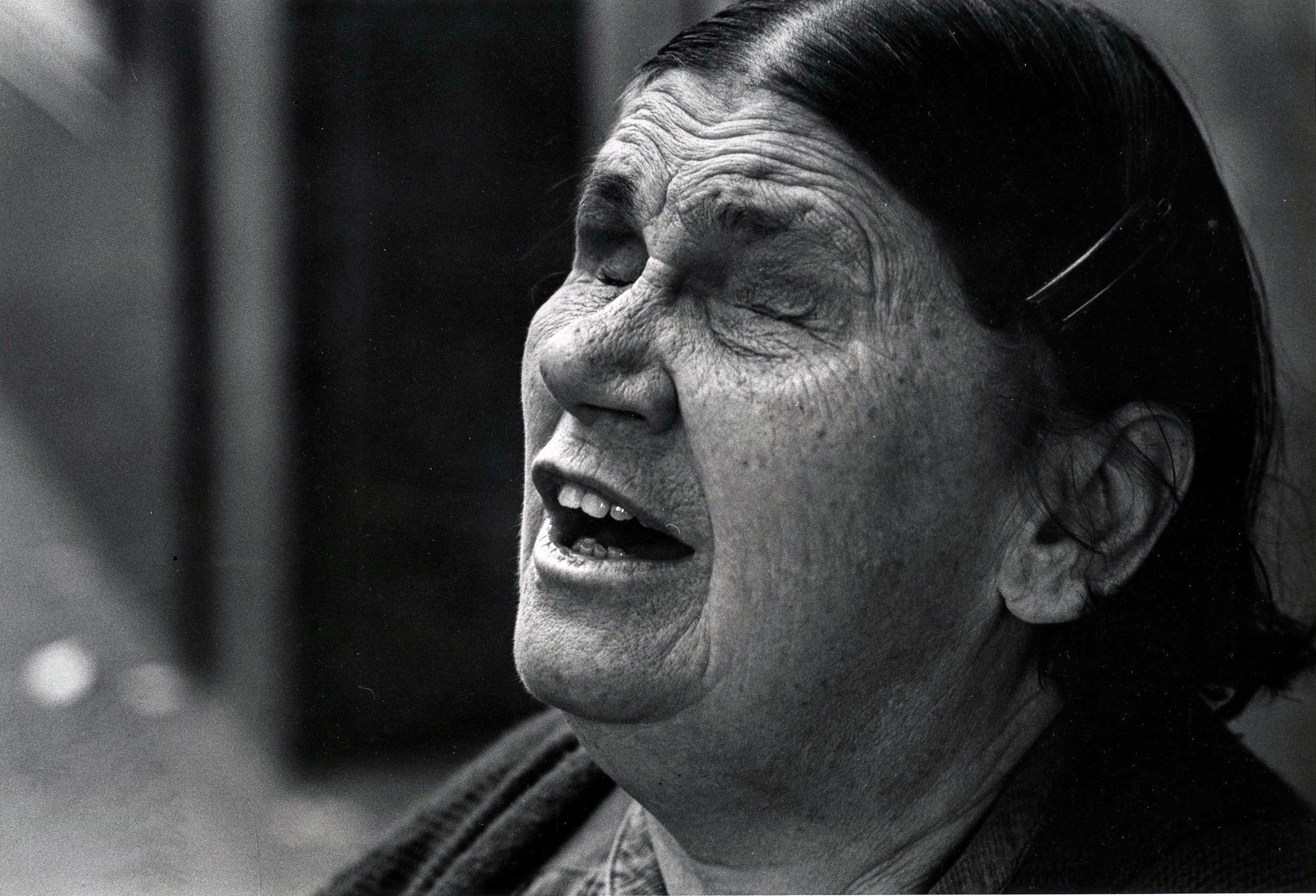 Elderly woman singing passionately with closed eyes.