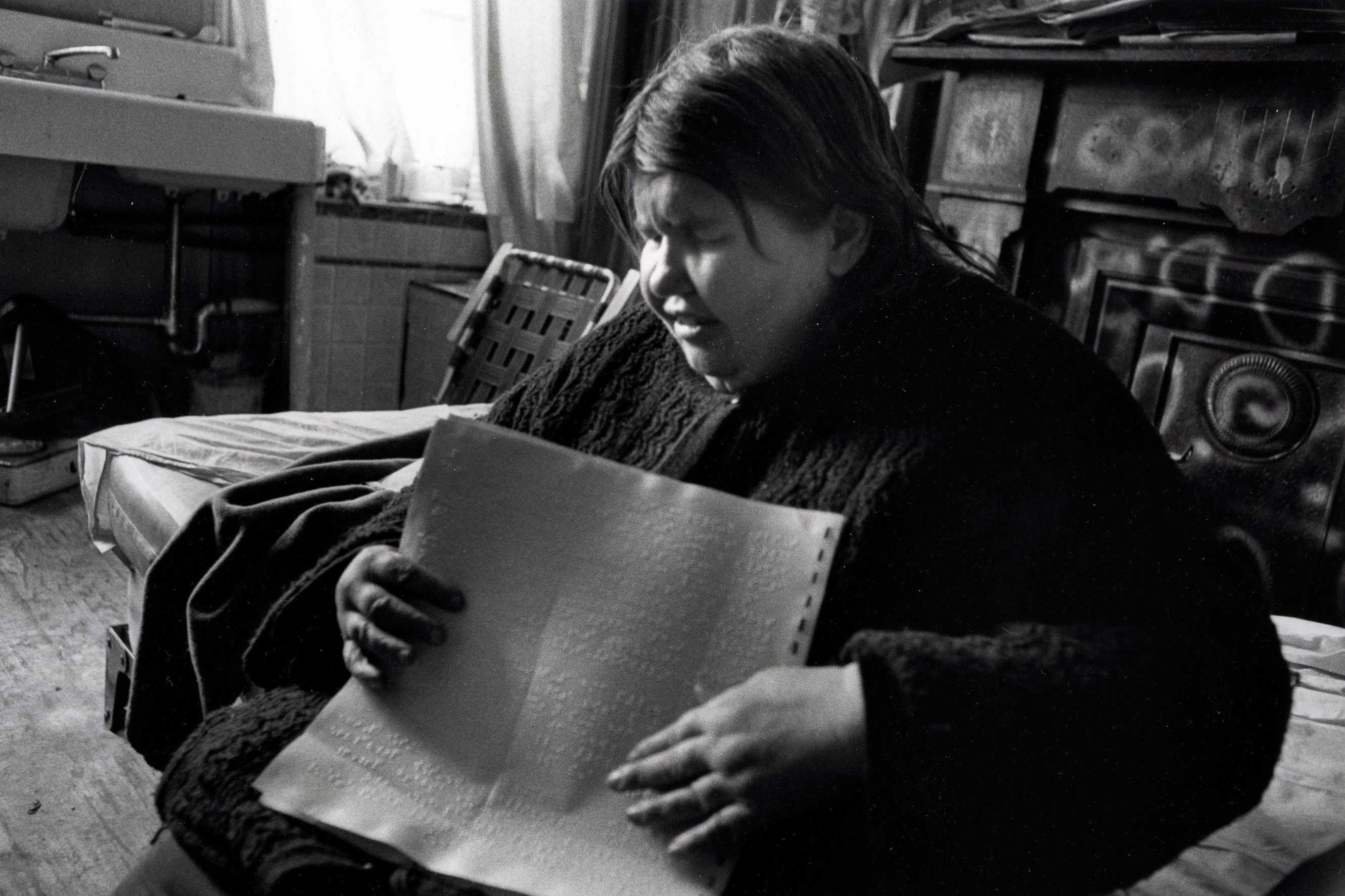Person reading Braille in dimly lit room.