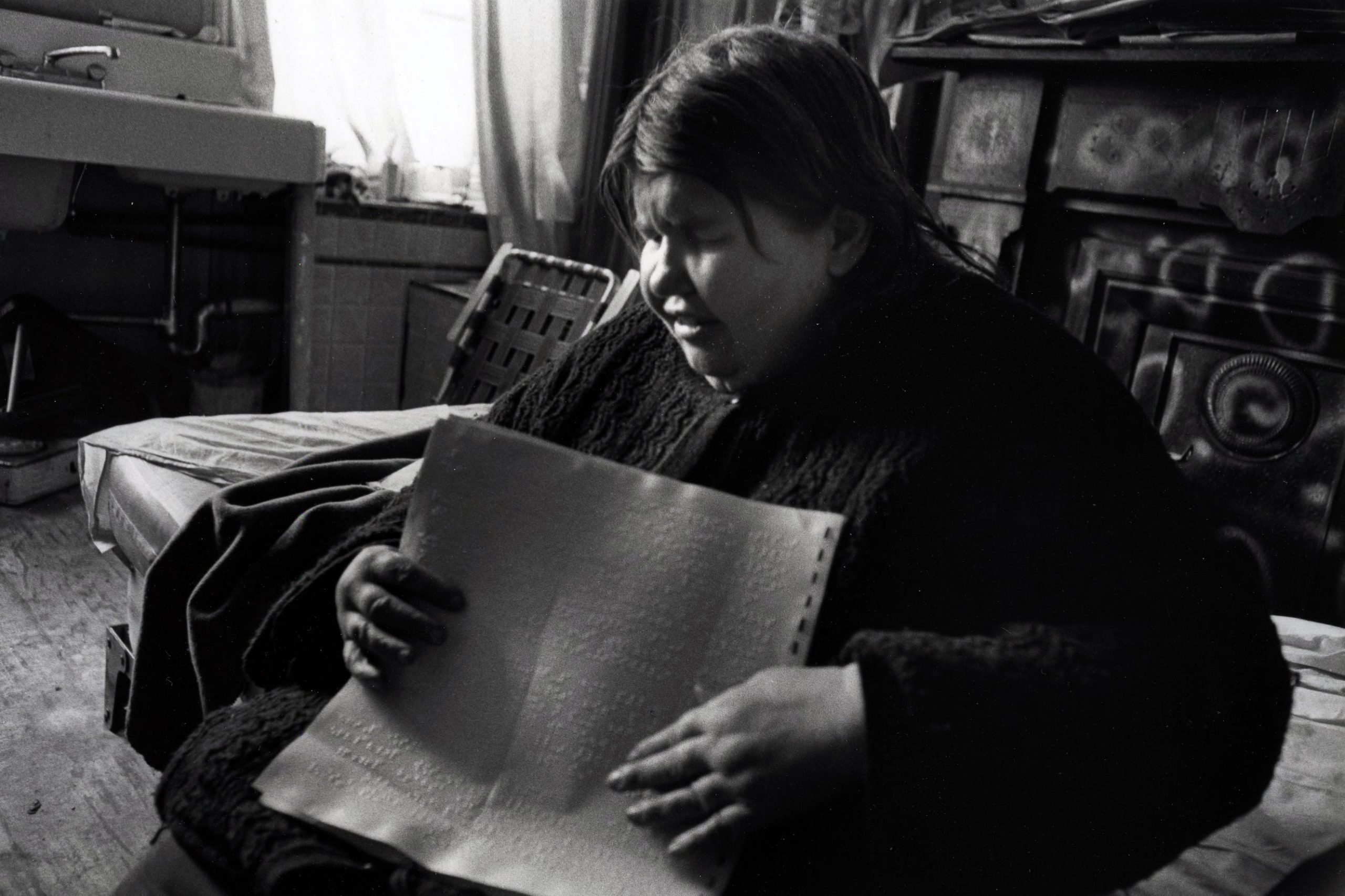 Person reading braille in dimly lit room.
