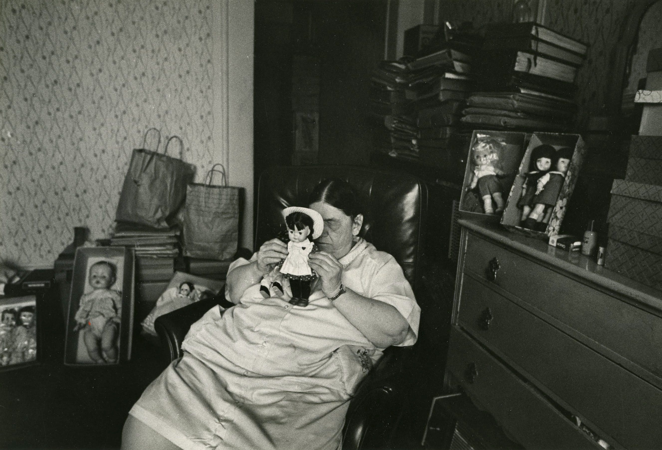 Woman holding doll in cluttered room.