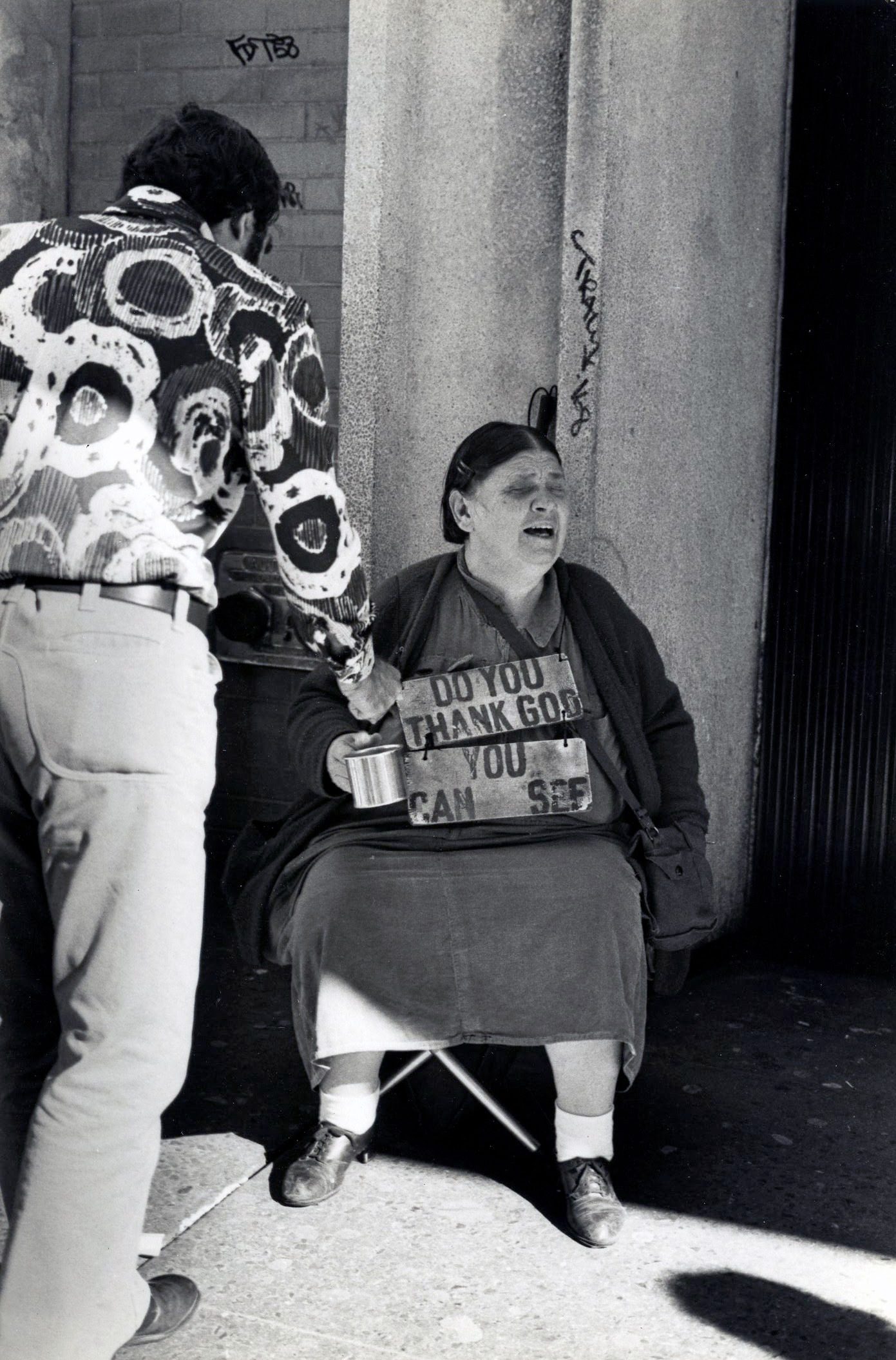 Man giving donation to seated woman outside.